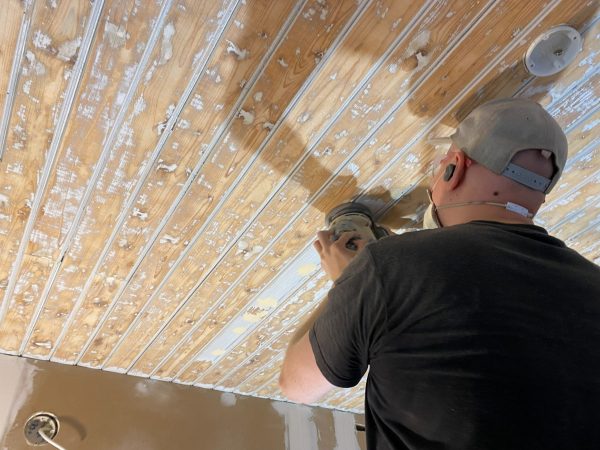 Mies hioo paneelikattoa ennen maalausta.