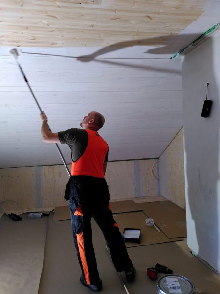 Mies maalaa sisäkattoa telalla.